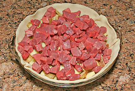 Add a layer of bite-sized beef cubes over the sliced potatoes.